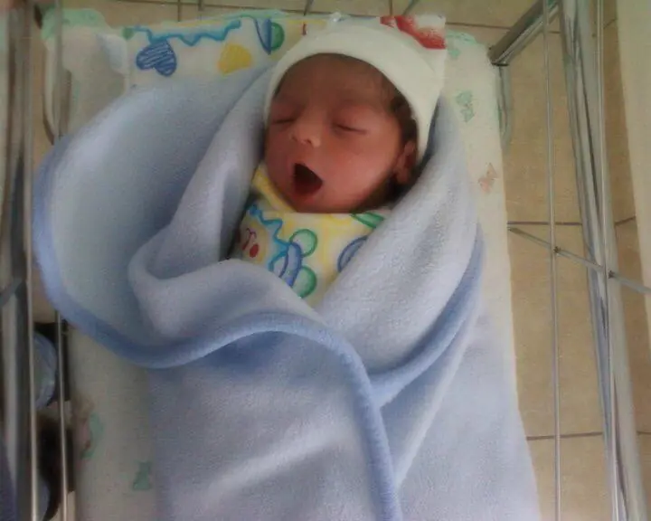 Adriel as a newborn, yawning, wrapped in a light blue blanket
