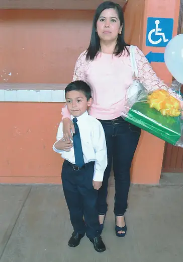 Adriel in a white shirt and tie next to his mother on graduation day