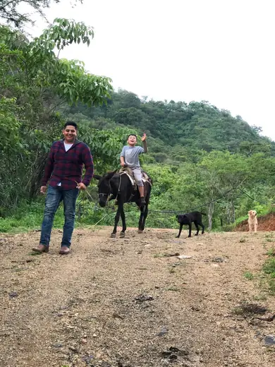 Adriel waving from a donkey led along a dirt road