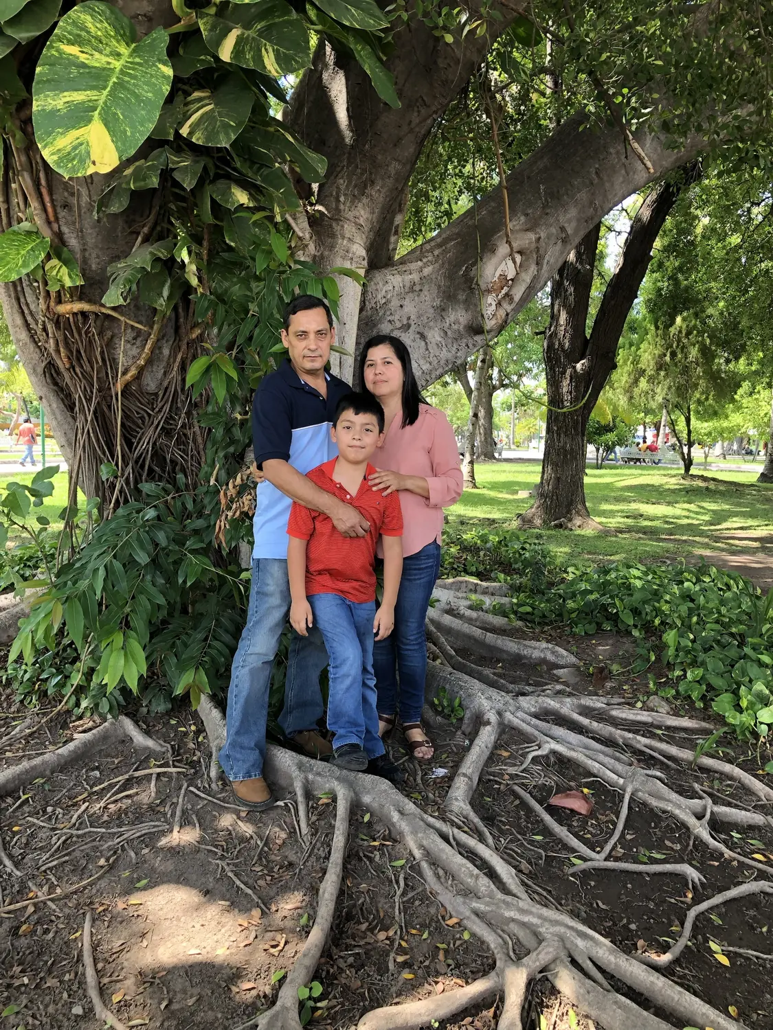 Adriel as a boy standing between his parents on the roots of a huge tree