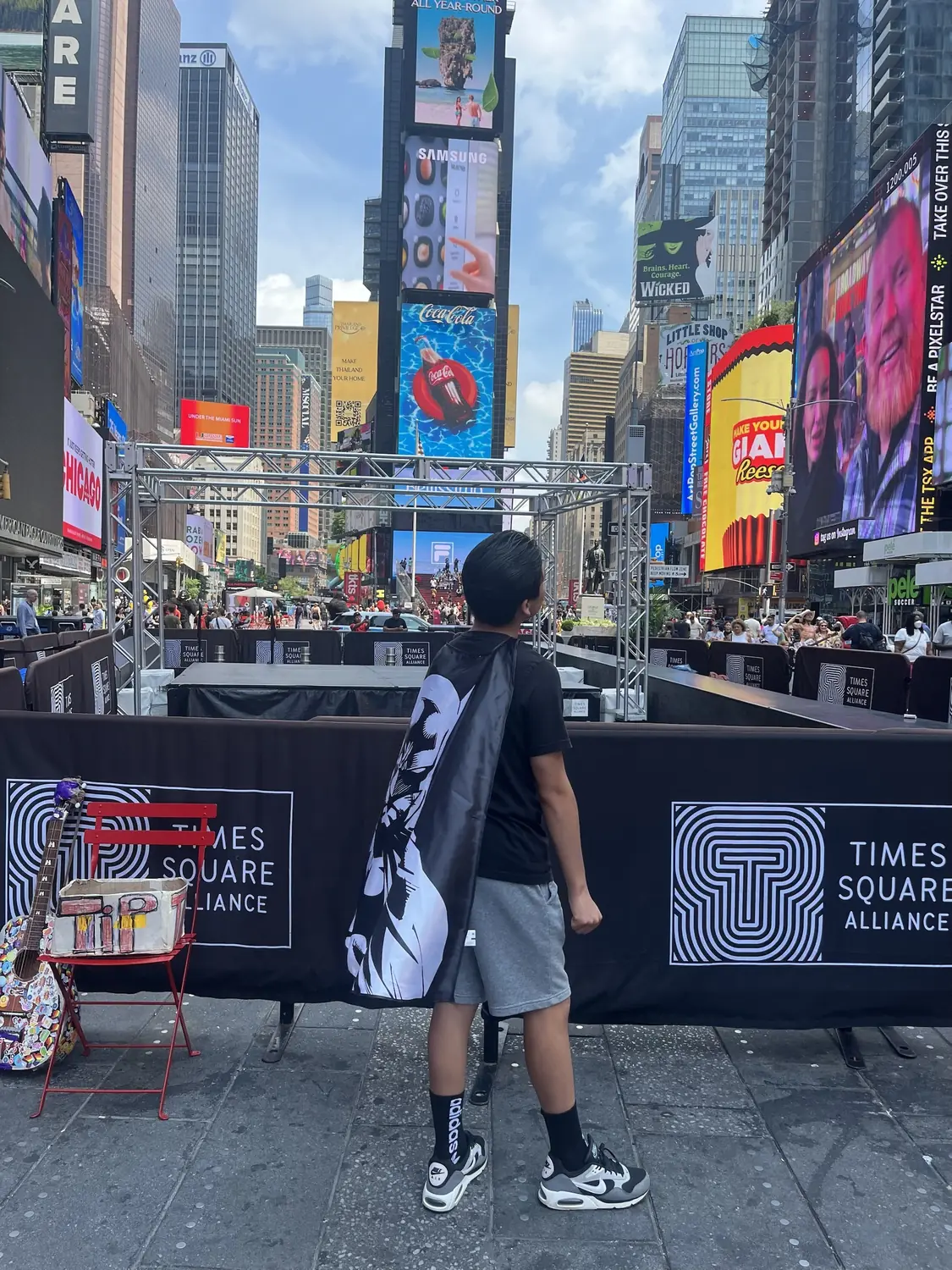 Adriel seen from behind in Times Square wearing a cape