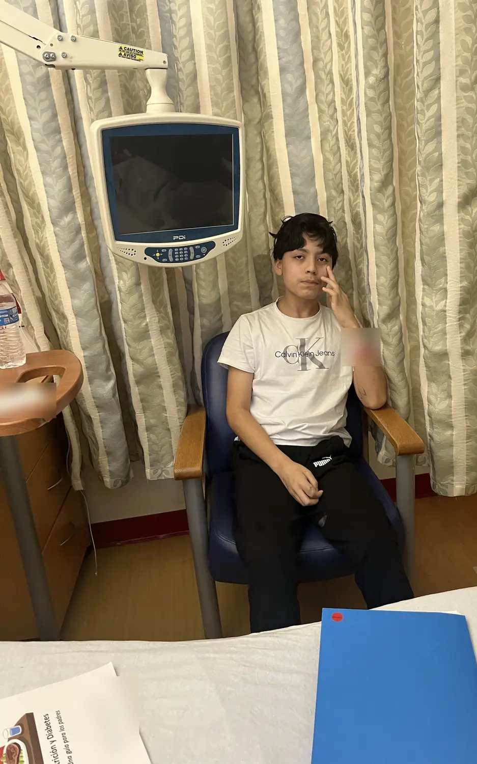 Adriel sitting in a hospital chair with a hand on his face, diabetes guides on the bed