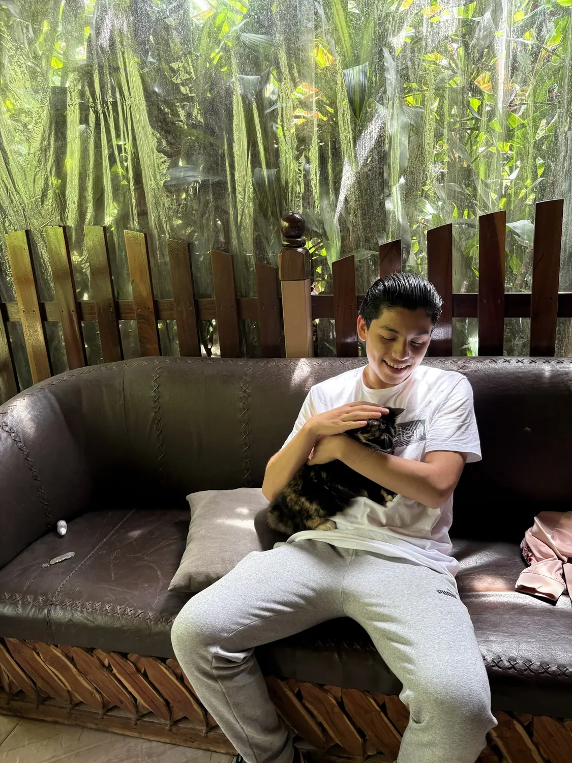 Adriel on a leather sofa smiling at a cat in his arms
